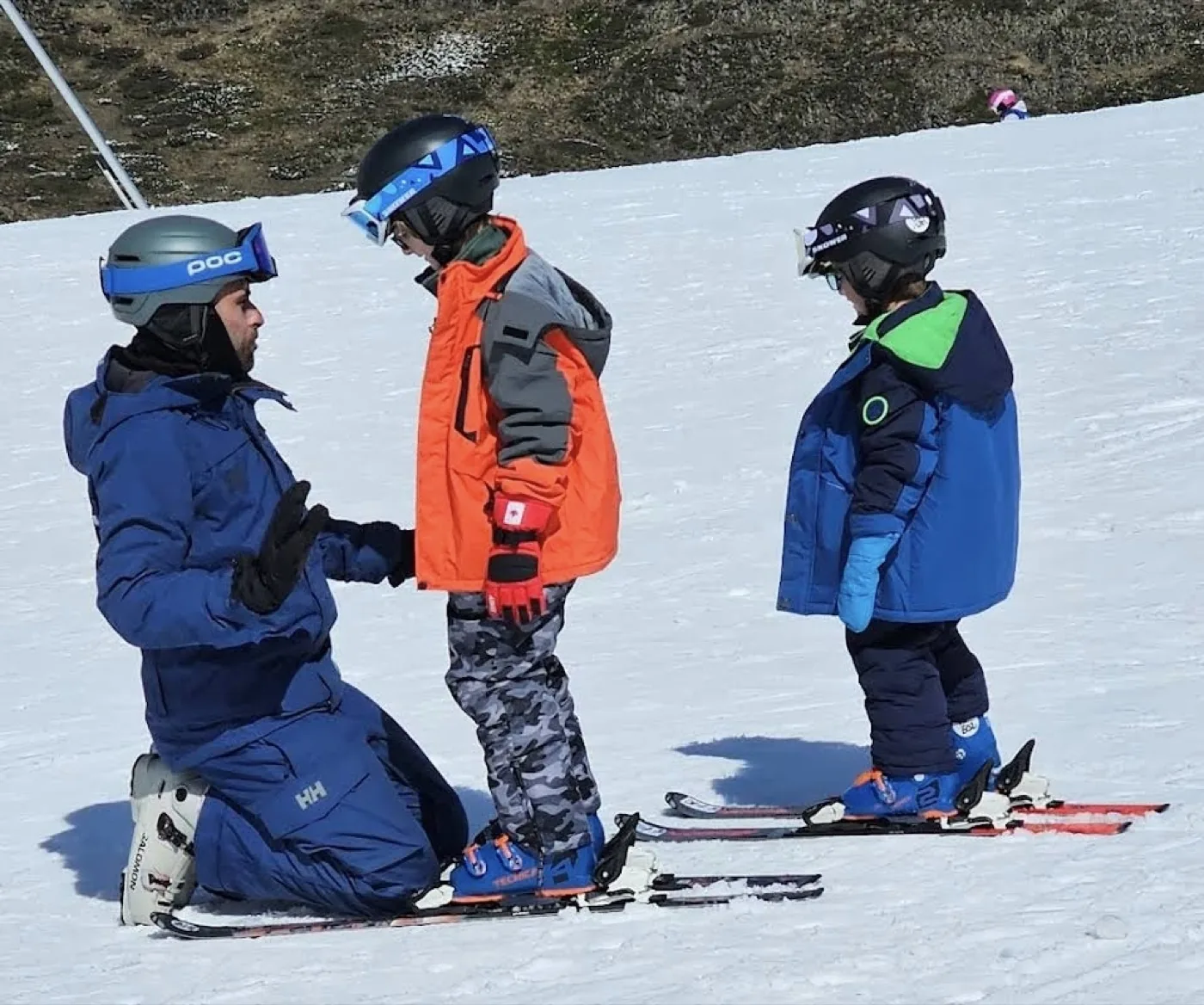 Profesor de esquí arrodillado dando indicaciones a dos niños en Baqueira-Beret