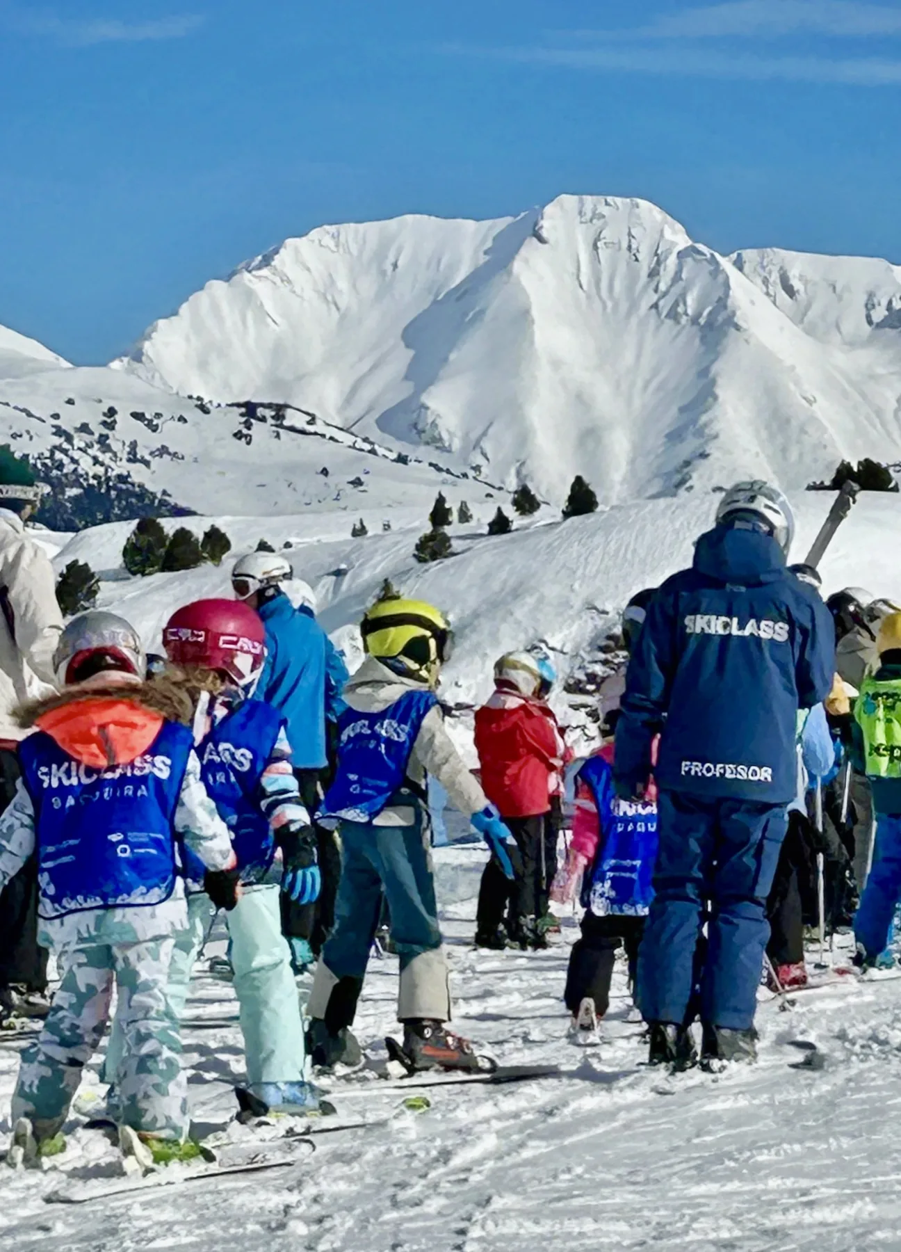 Groupe de cours collectif de ski pour enfants avec son moniteur face aux montagnes de Baqueira